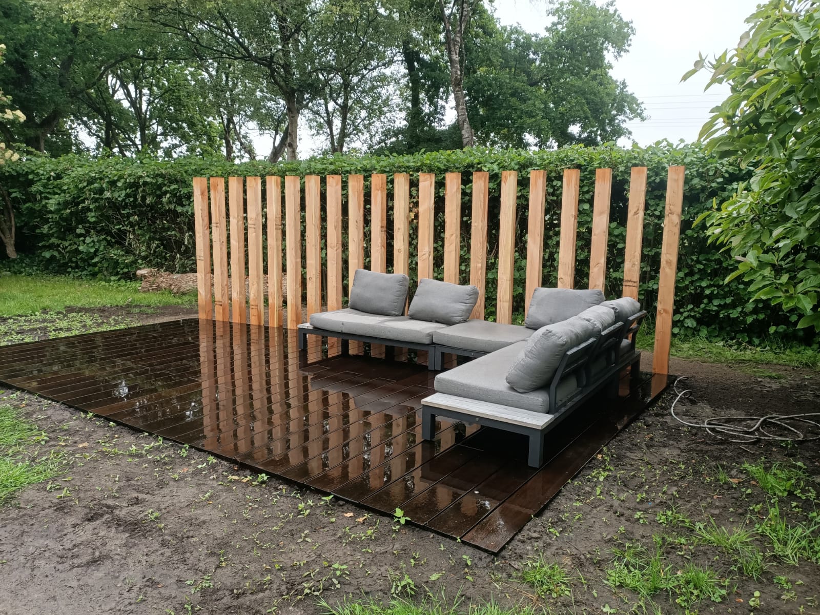 Donker houten vlonderterras met loungeset en lattenscherm