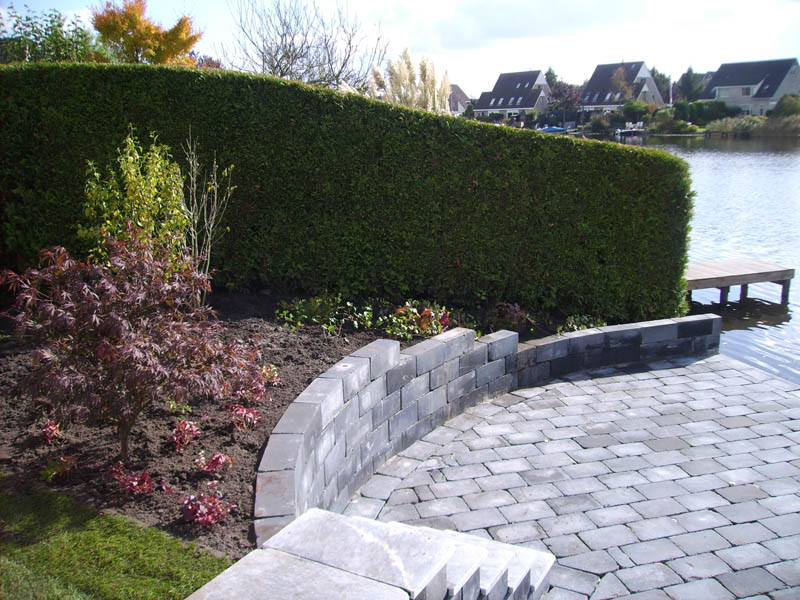 Gebogen terras met keerwand en haag aan het water